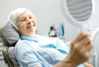 gray-haired woman admiring her smile in hand mirror