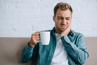 person with a toothache holding a cup of coffee