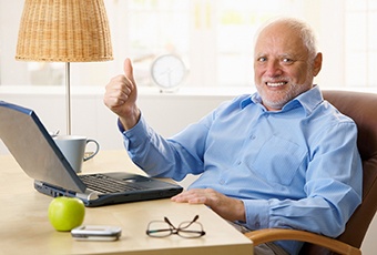 Senior man sitting at laptop giving a thumbs up