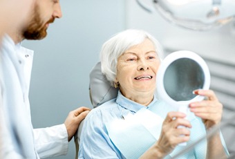 Senior woman using mirror to admire her implant dentures