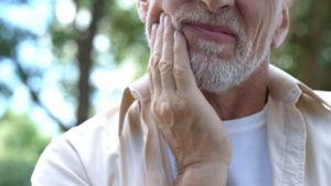 older man holding touching painful jaw 